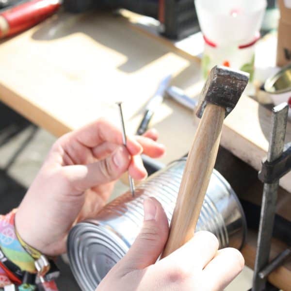 Symbolbild für Upcycling: ein Nagel soll mit einem Hammer in eine Blechbüchse beschlagen werden